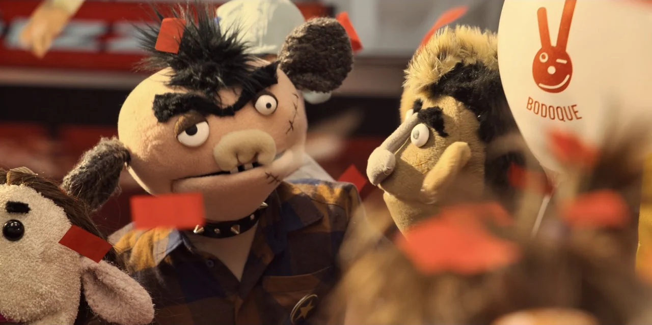 31 Minutes: One Hot Christmas (2025) movie still: medium — A cluttered retail interior features multiple plush puppets arranged on a shelf. A brown…