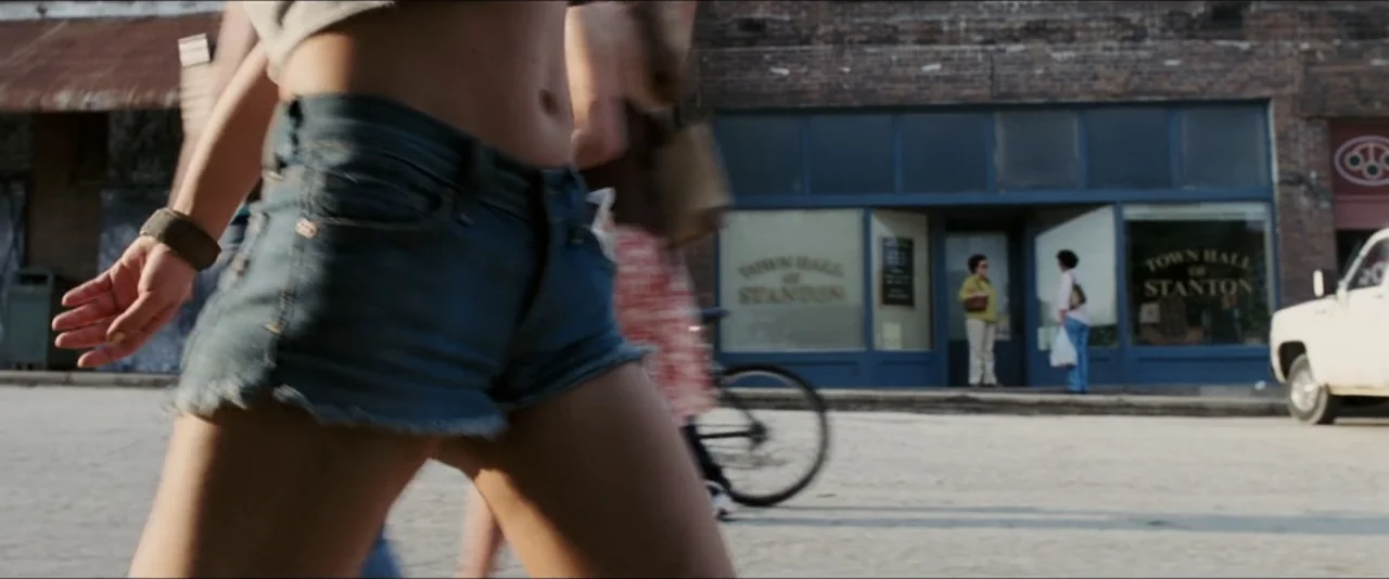 Black Snake Moan (2006) movie still: medium — A small town square features an old brick town hall building in background. A person in denim shorts…
