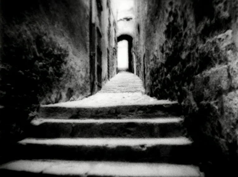 Cuadecuc, Vampir (1971) movie still: establishing — A narrow, stone-walled staircase leads upwards towards a bright, arched passage in the distance.…
