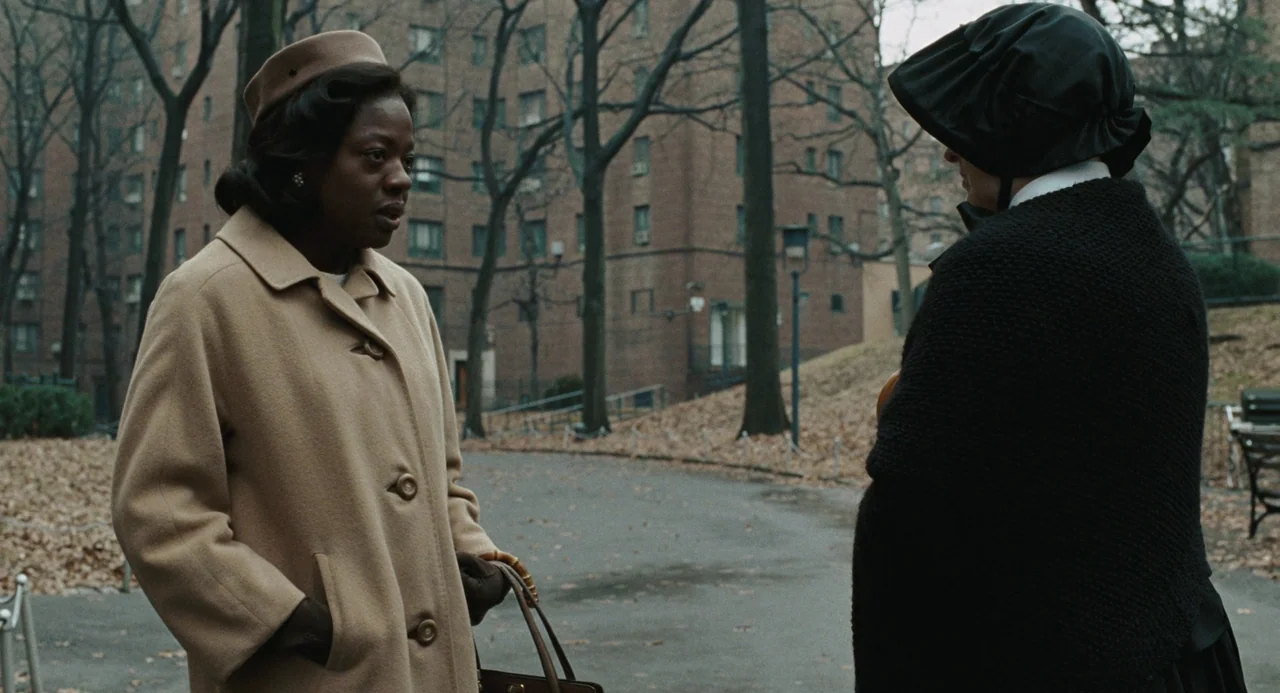 Doubt (2008) movie still: medium — Two women stand in a public area with brick apartment buildings visible behind trees. The woman in beige talks…