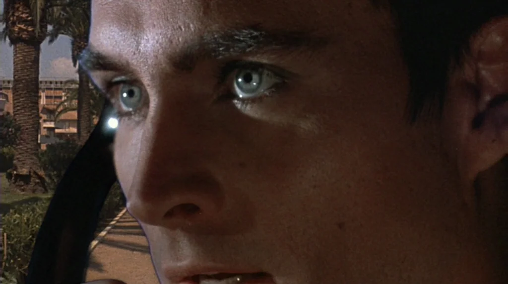 Danger Diabolik (1968) movie still: closeup — A man's face is shown in close-up with palm trees in the blurred background. The subject is looking…