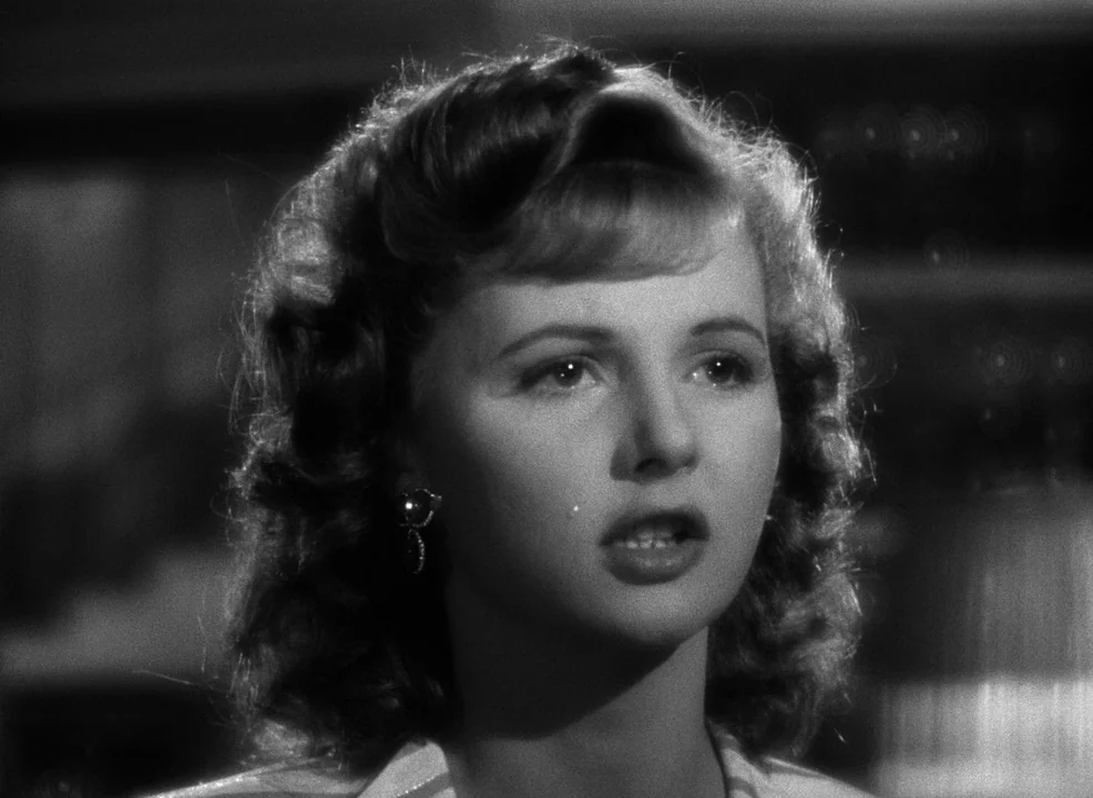 Casablanca (1942) movie still: closeup — A dimly lit indoor space with blurred shapes in the background. A young woman with wavy hair turns her head…