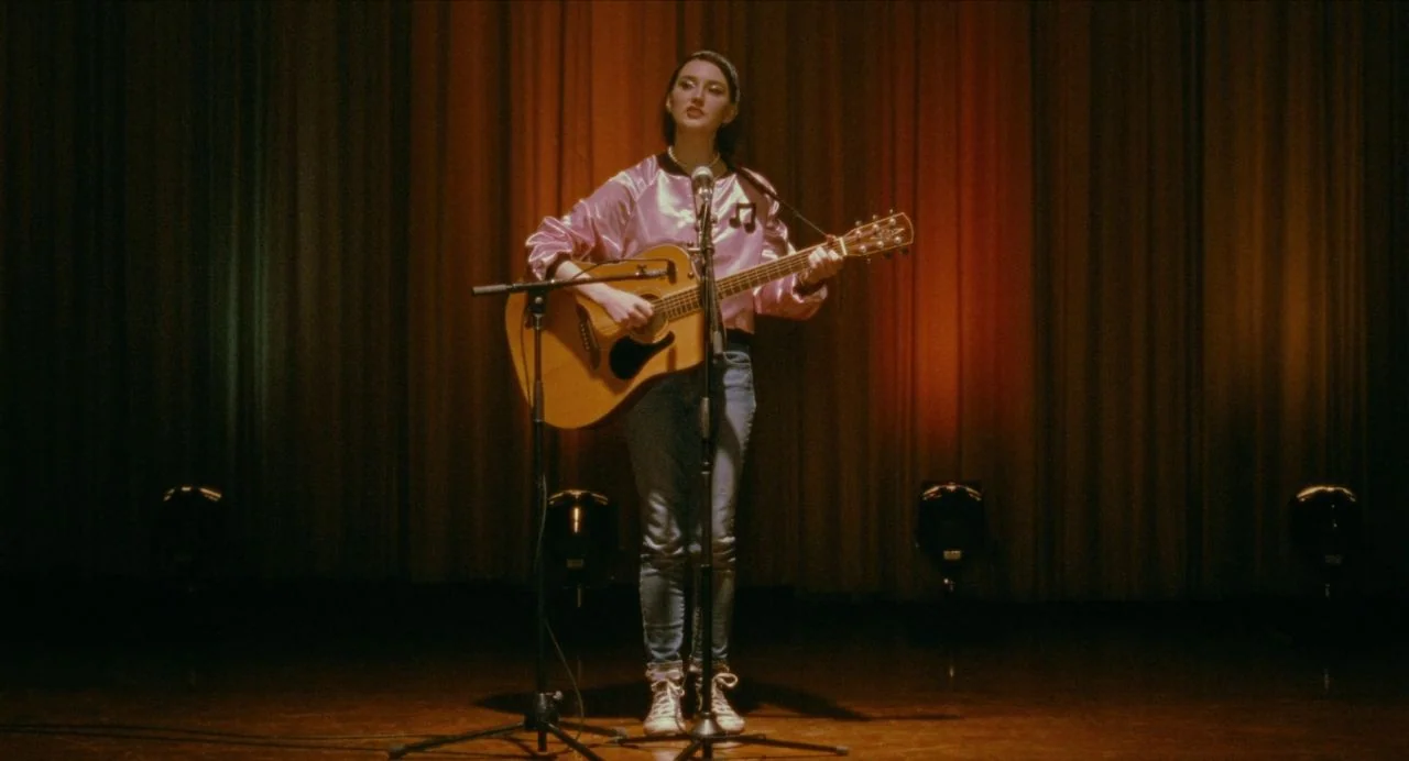 Never Rarely Sometimes Always (2020) movie still: fullbody — A performer stands center on a dark, wood-floored stage before thick velvet curtains.…