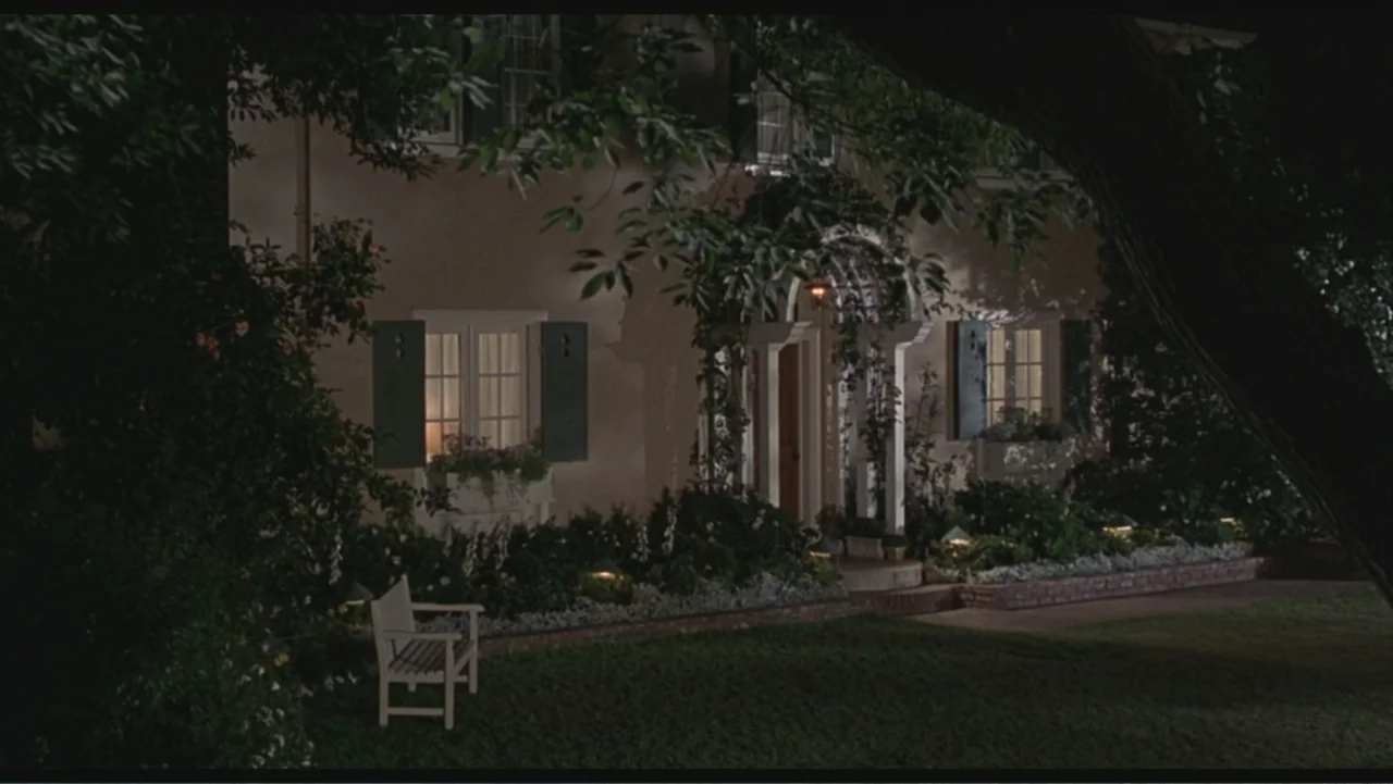 Liar Liar (1997) movie still: establishing — A two-story traditional house with green shutters is surrounded by overgrown trees and shrubs. A white…
