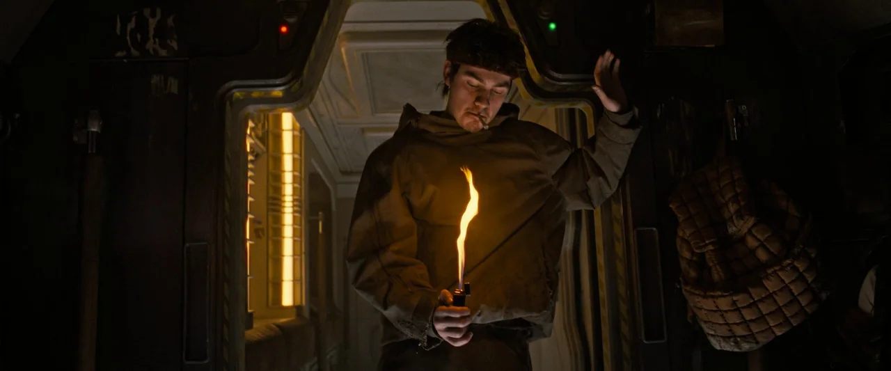 Alien: Romulus (2024) movie still: medium — A dimly lit metallic passageway on a spacecraft featuring recessed paneling and illuminated status…