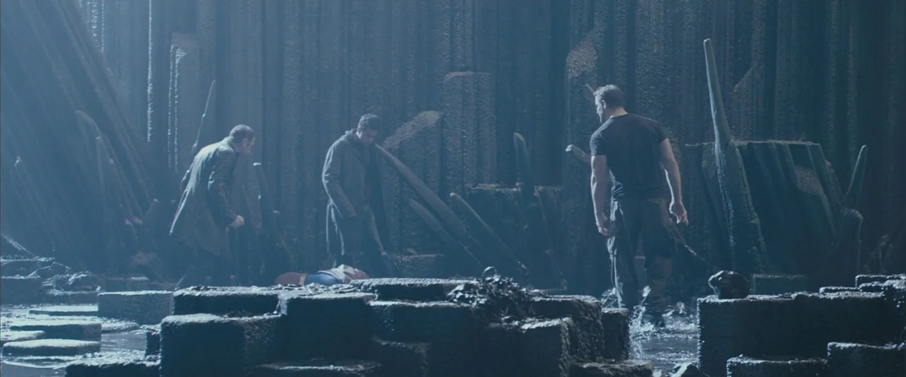 Superman Returns (2006) movie still: wide — A dark subterranean cavern features jagged vertical stone columns and pools of shallow water. Three men…