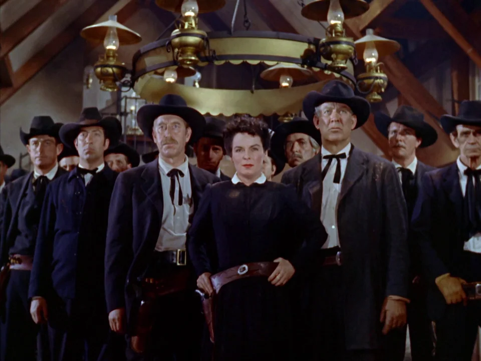 Johnny Guitar (1954) movie still: medium — A rustic barn interior features exposed wooden rafters and a hanging circular light fixture. A woman in a…
