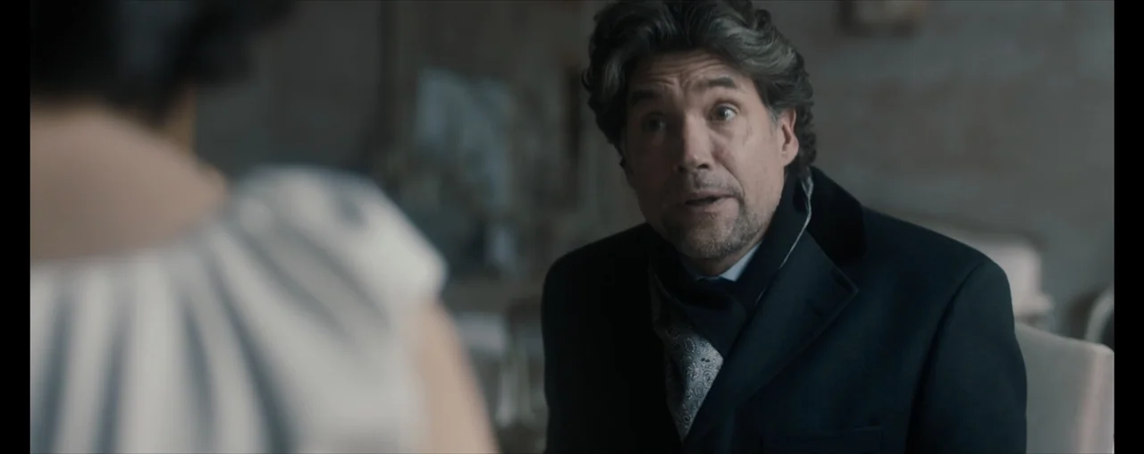 The Wrong Tenant (2022) movie still: medium — An interior space with muted colors and a classic, somewhat formal arrangement. A man in a dark coat…