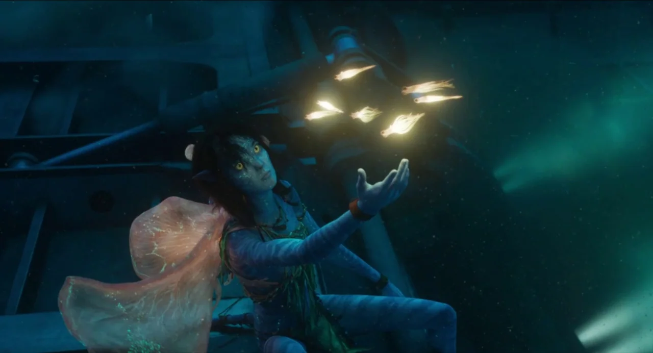 Avatar: The Way of Water (2022) movie still: medium — A blue-skinned humanoid character floats underwater near a dark metallic structure. She…