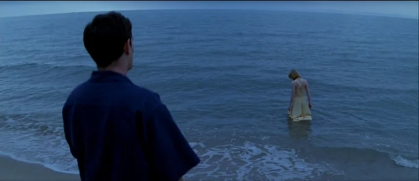 The Thin Red Line movie still: wide — An expanse of calm ocean meets a sandy shore during twilight. A man in the foreground observes a woman…