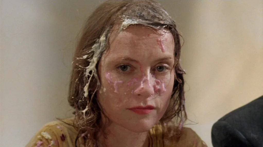 Malina (1991) movie still: closeup — A light-colored interior setting frames the subject. A woman stares forward with thick food substances covering…