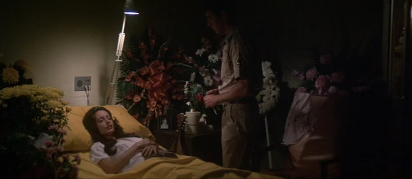 Nashville (1975) movie still: medium — A dimly lit funeral parlor displays an open casket with large flower arrangements nearby. A man in military…