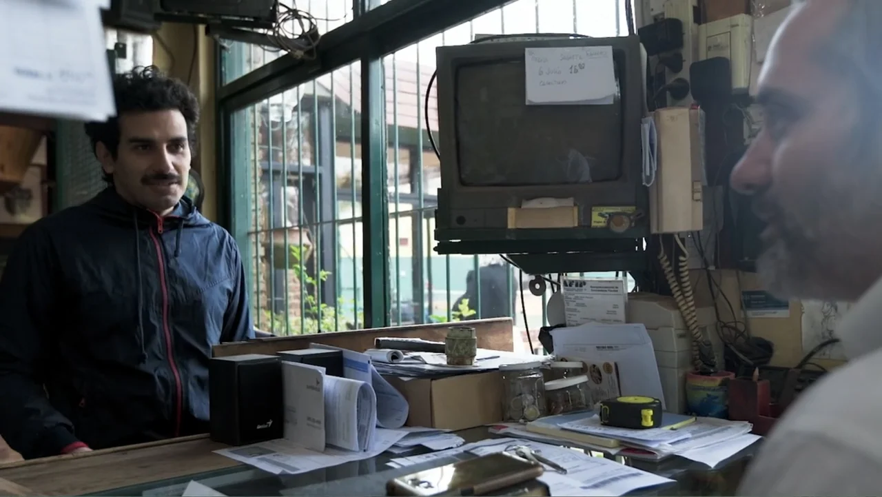 Smog in Your Heart (2022) movie still: medium — A cluttered service counter in a small shop is filled with papers, old electronics, and office…