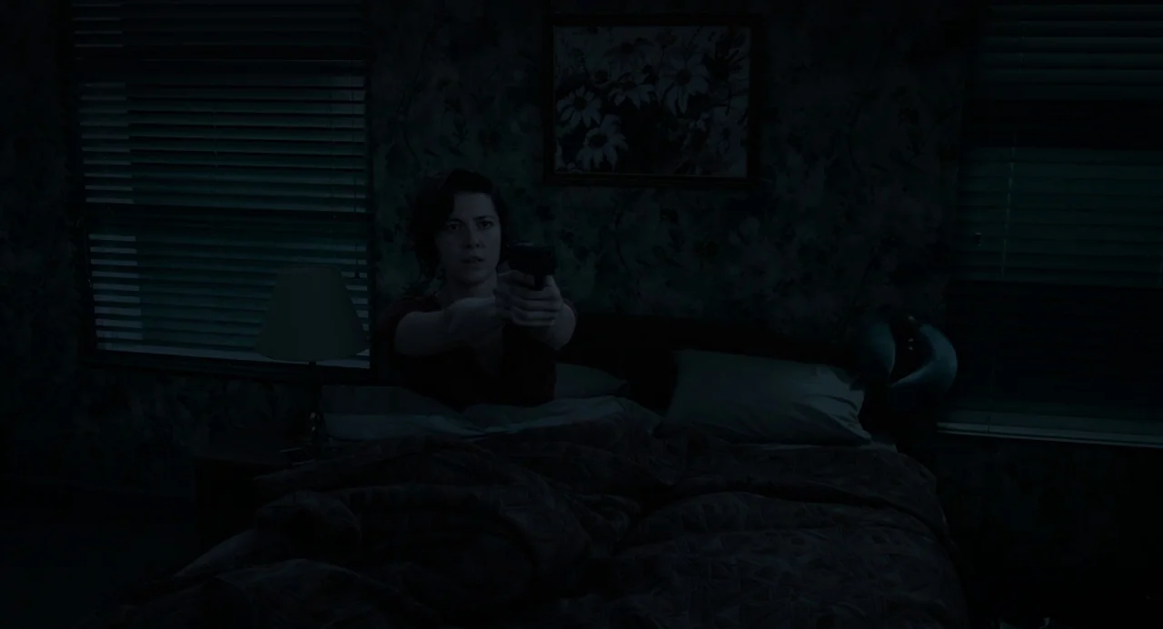 Gemini Man (2019) movie still: medium — A dark bedroom with patterned wallpaper, a framed floral print, and Venetian blinds. A woman sits upright in…