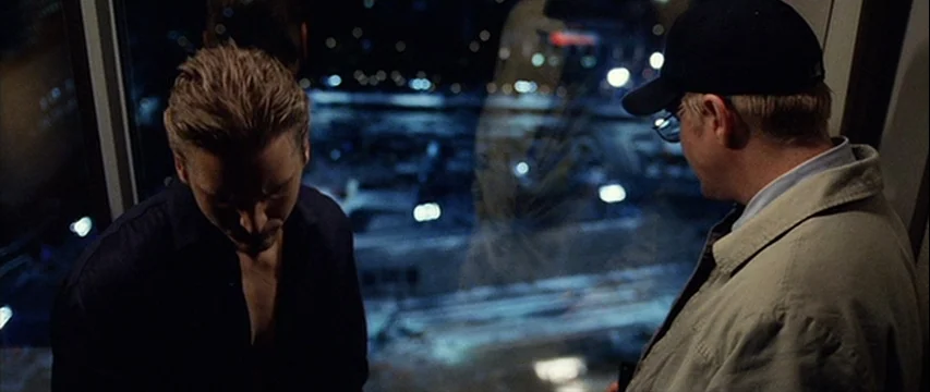 25th Hour (2002) movie still: medium — A dark, modern high-rise interior features a floor-to-ceiling glass window overlooking city lights. Two men…