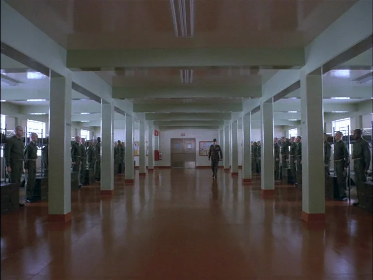 Full Metal Jacket (1987) movie still: wide — A spacious military barracks features rows of support pillars and polished brown linoleum floors. A…