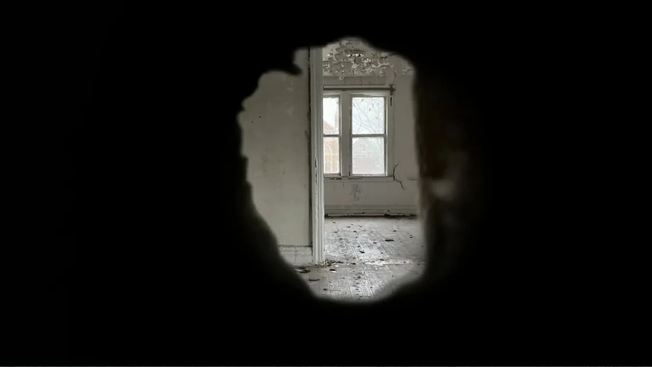 Inland Empire (2006) movie still: establishing — A dilapidated room viewed through a large irregular hole in a wall. The space contains debris on…