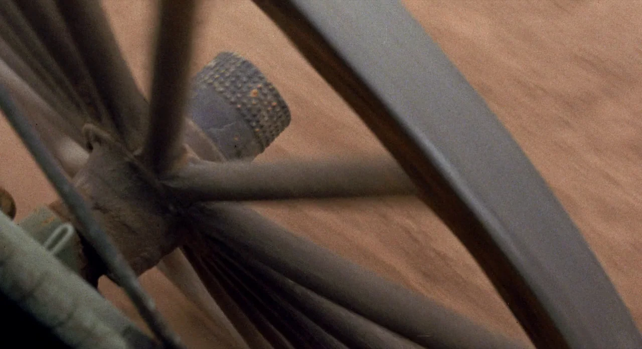Ride In The Whirlwind (1966) movie still: closeup — A close-up view shows a metal wagon wheel spinning against a blurred dirt road. The central hub…