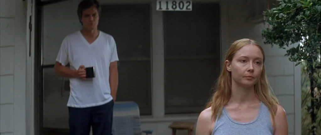 Shotgun Stories (2007) movie still: medium — A suburban house exterior with white siding and a visible street number sign. A woman in a grey tank…