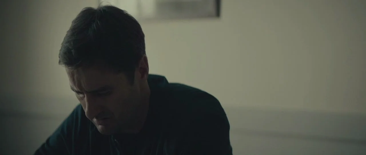 Meadowland (2015) movie still: medium — A spartan office environment features muted wall colors and an indistinct framed picture. A middle-aged man…