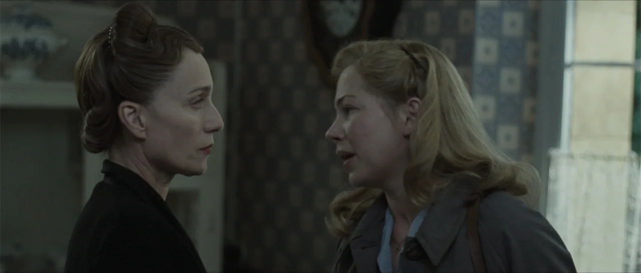 Suite Française (2015) movie still: medium — A 1940s-style domestic interior features patterned wallpaper and antique furniture. Two women stand in…