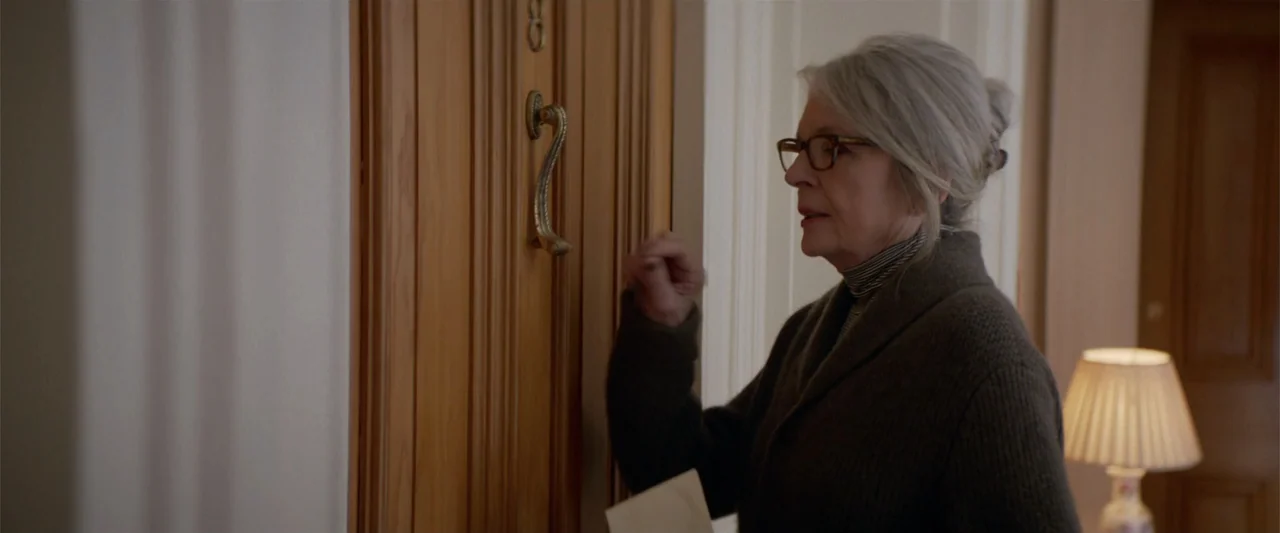 Hampstead (2017) movie still: medium — A woman stands in a hallway beside a wooden door with a metal knocker. She is knocking on the door while…