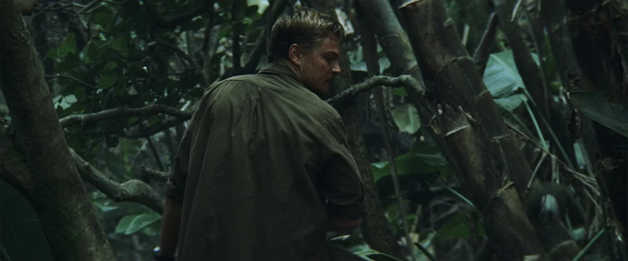 Blood Diamond (2006) movie still: medium — A dense, overgrown jungle environment filled with thick bamboo stalks and layered green foliage. A man in…