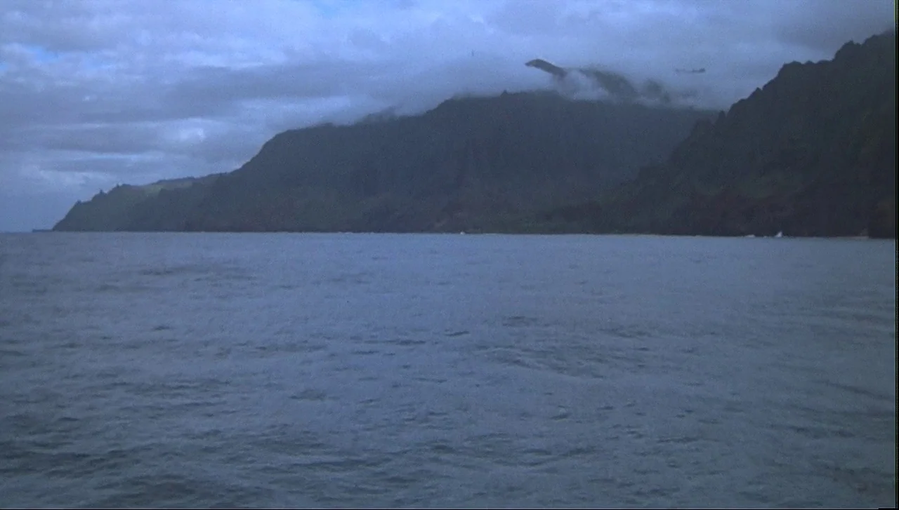 The Lost World: Jurassic Park (1997) movie still: establishing — A vast expanse of dark ocean meets a large, jagged coastline under a cloudy sky.…