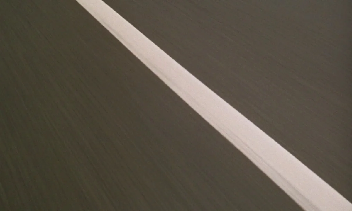 If…. (1968) movie still: establishing — An asphalt road surface extends across the frame with a diagonal white line. The texture of the pavement is…