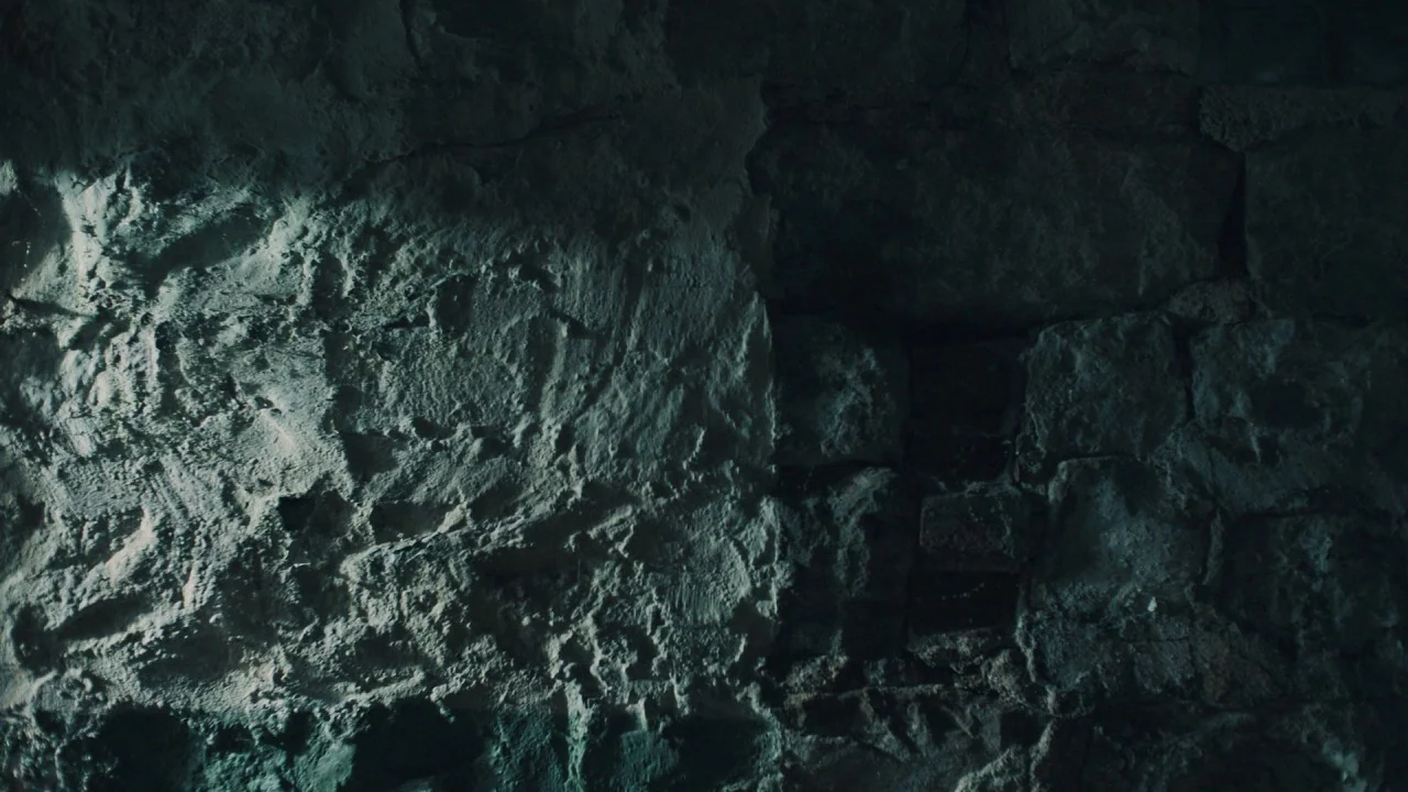 Girl on the Third Floor (2019) movie still: closeup — A close-up view of a rugged stone wall with visible mortar and uneven surfaces. Harsh side…