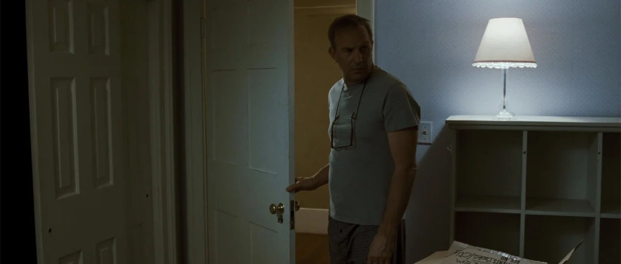 The New Daughter (2009) movie still: medium — A man stands in a dimly lit hallway next to an open door. The man turns his head to look into the room…