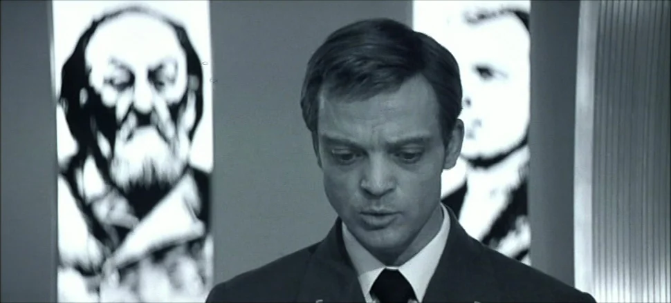 Solaris (1972) movie still: medium — A minimalist interior contains glowing vertical panels displaying large, high-contrast portraits of men. A man…