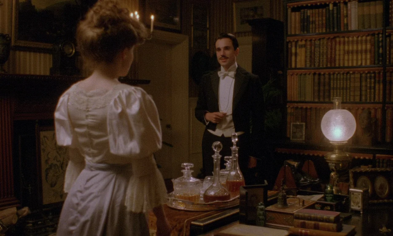 A Room With A View (1985) movie still: medium — A dark, wood-paneled room features tall bookshelves and a lit table lamp. A woman faces a man in…