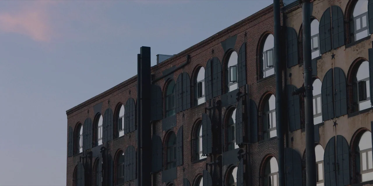 Hearts Beat Loud (2018) movie still: establishing — A multi-story historic brick building features numerous arched windows with dark metal shutters.…