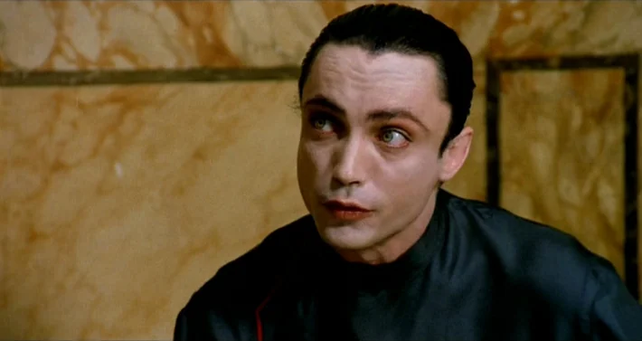 Blood For Dracula (1974) movie still: closeup — A man stands in front of a wall with veined yellow marble panels. He looks slightly off-camera with…