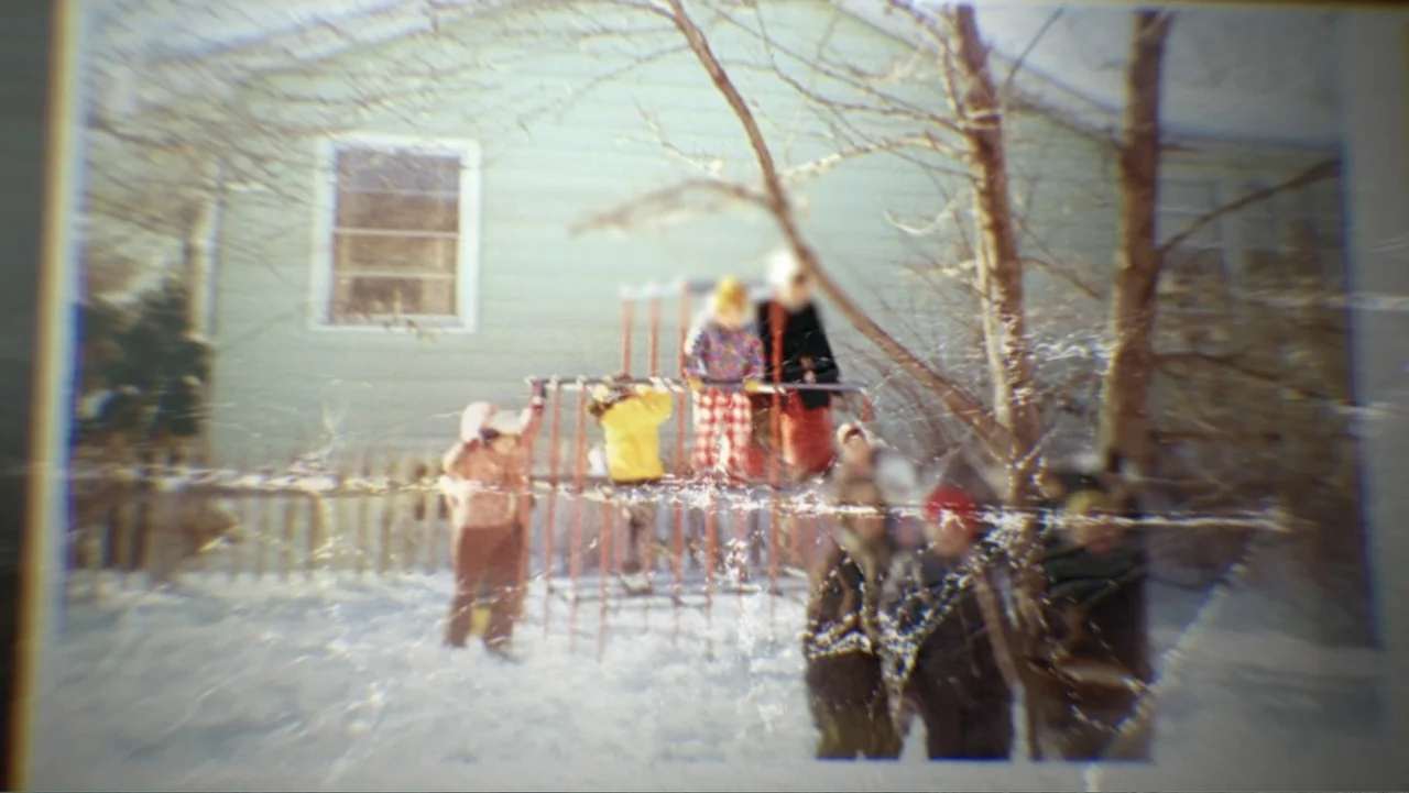 What Happened at Fells Acres? (2023) movie still: wide — A snowy backyard features a metal jungle gym set against the side of a house. Several…
