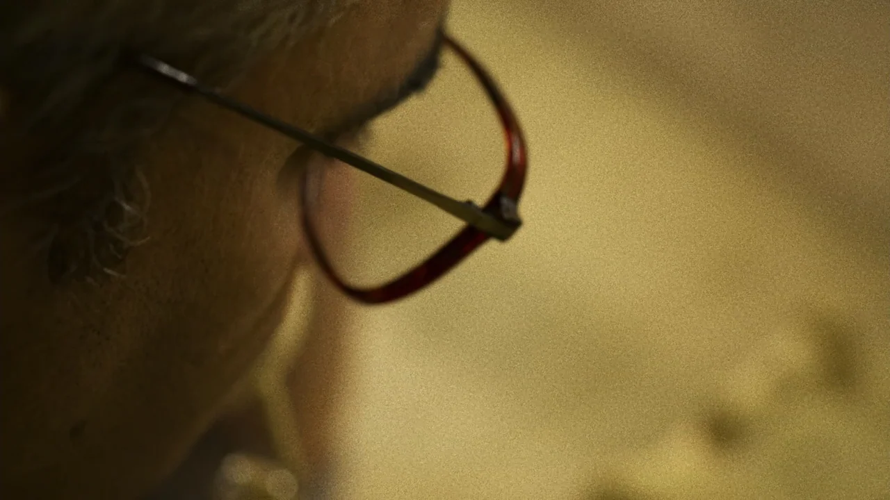 An Affair: A Dangerous Sexual Play (2014) movie still: closeup — A dimly lit workspace features a person seen from the side in tight focus. The…
