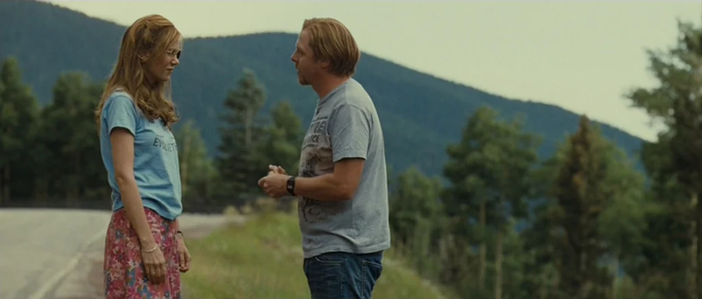 Paul (2011) movie still: fullbody — A roadside beside a large mountain range under a pale sky. The two people stand facing each other on the…