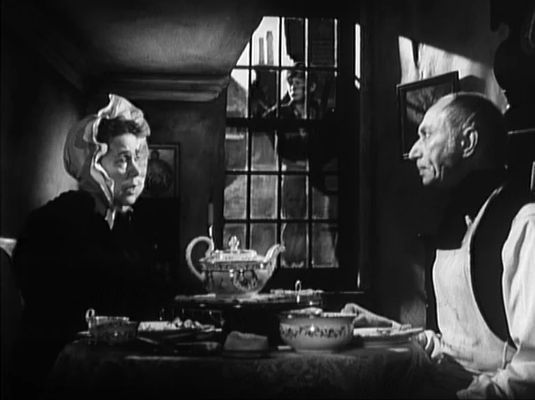 Oliver Twist (1948) movie still: medium — An interior space with a set table near a large, multi-paned window. A man and a woman sit facing each…