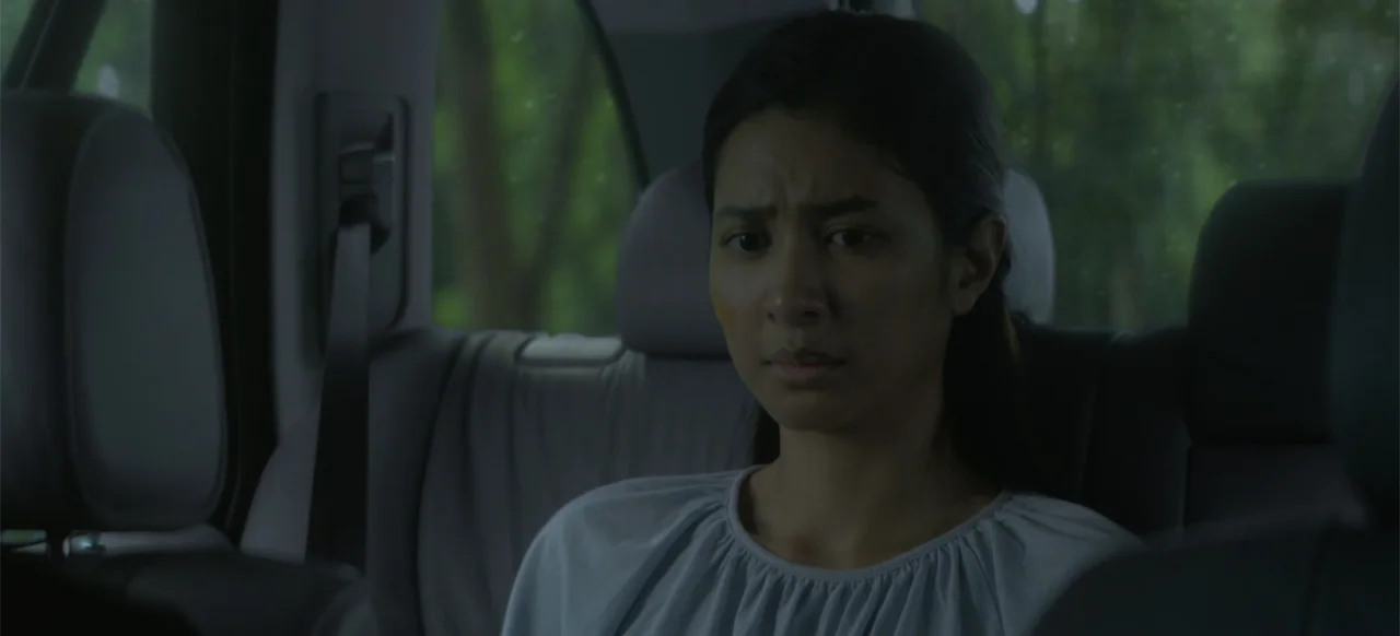 A Thousand Days (2023) movie still: medium — The interior of a car shows a backseat with grey headrests and seatbelts. A young woman sits in the…