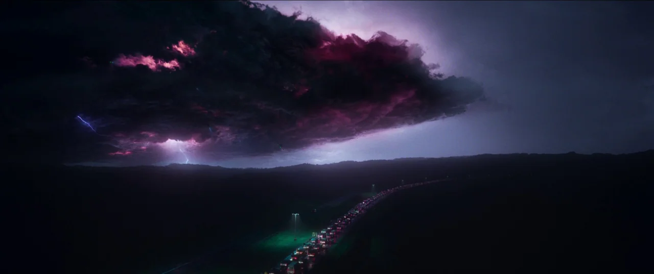 White Noise (2022) movie still: establishing — A dark night landscape features a congested highway winding through a silent, unlit area. A massive…