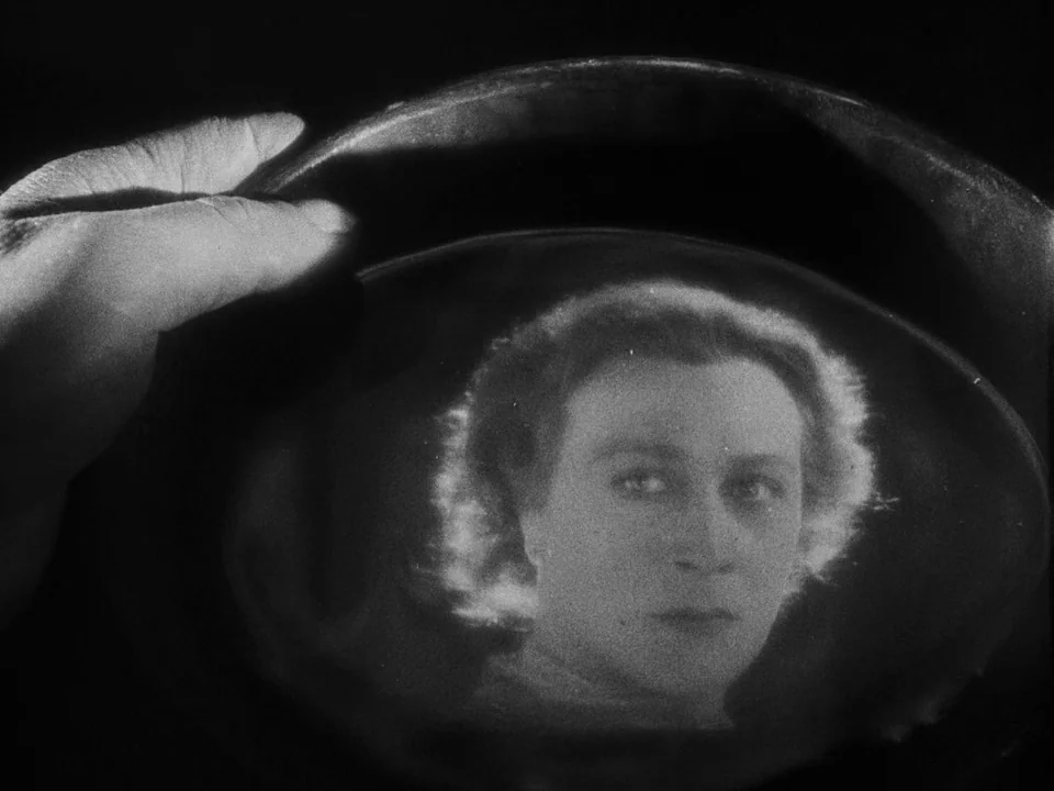 Faust (1926) movie still: closeup — A close-up of a hand holding a dark vessel in a pitch-black environment. The curved surface of the vessel…
