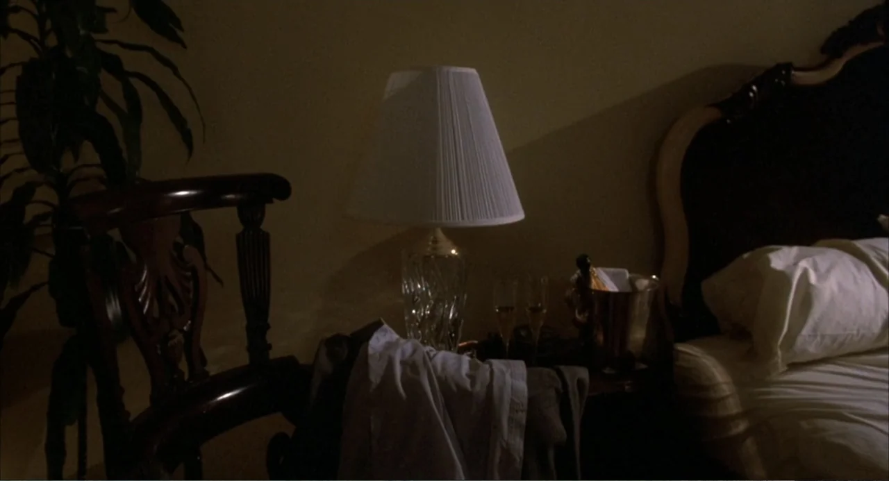 Murphy's Law (2009) movie still: medium — A dimly lit hotel bedroom features a bedside lamp casting light on a nightstand. A bed is visible to the…
