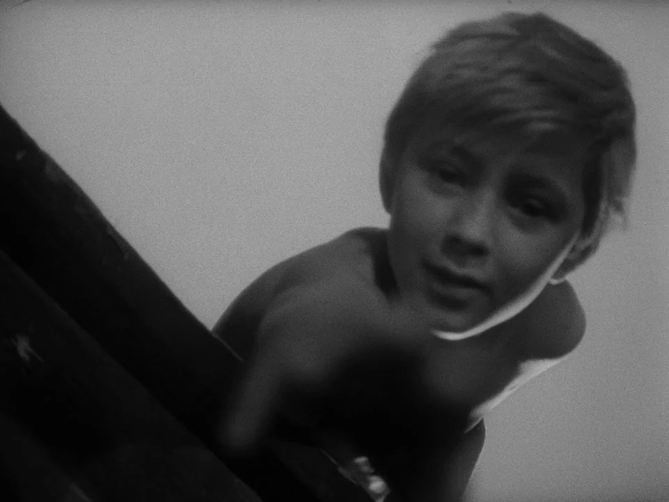 Ivan’s Childhood (1962) movie still: closeup — An outdoor structure made of wooden planks appears against a neutral background. A young boy leans…