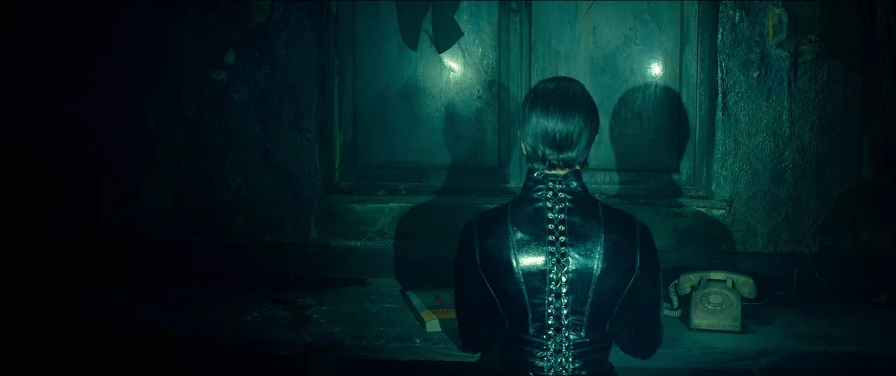 The Matrix Resurrections (2021) movie still: medium — A dark, dilapidated interior features a worn desk set against a large window. A figure sits at…