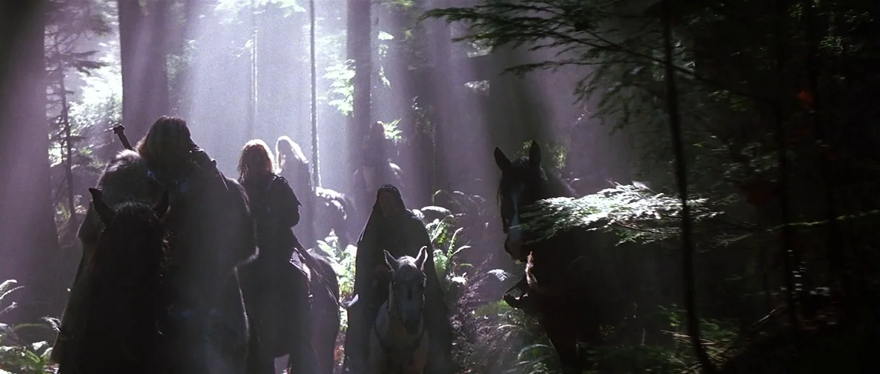 The 13th Warrior (1999) movie still: wide — A group of riders on horseback moves through a thick, ancient growth forest area. Beams of light filter…