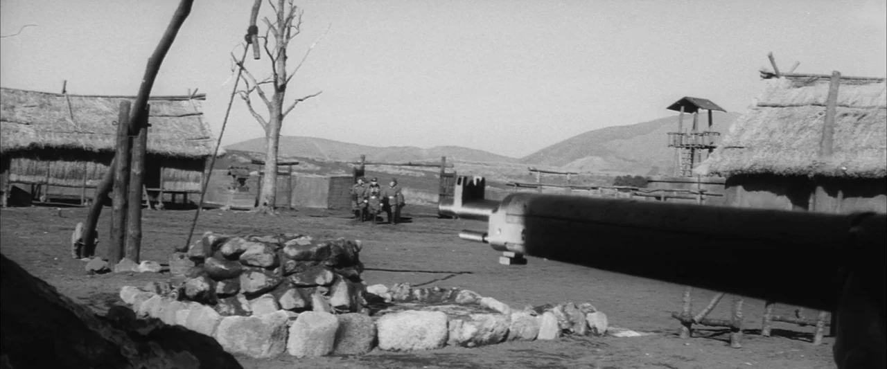 The Human Condition III: A Soldier’s Prayer (1961) movie still: wide — A rural settlement features thatched huts, a stone well, and a distant guard…