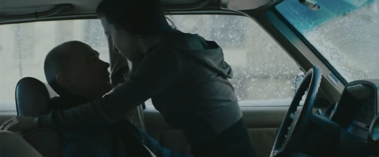 Anora (2024) movie still: medium — The interior of a car during a snowy day is visible through the window. A woman leans across the center console…