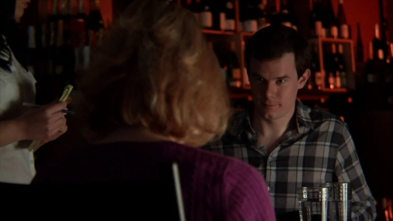 A Horrible Way To Die (2010) movie still: medium — A dimly lit restaurant interior features shelves of wine bottles against a deep red wall. A man…