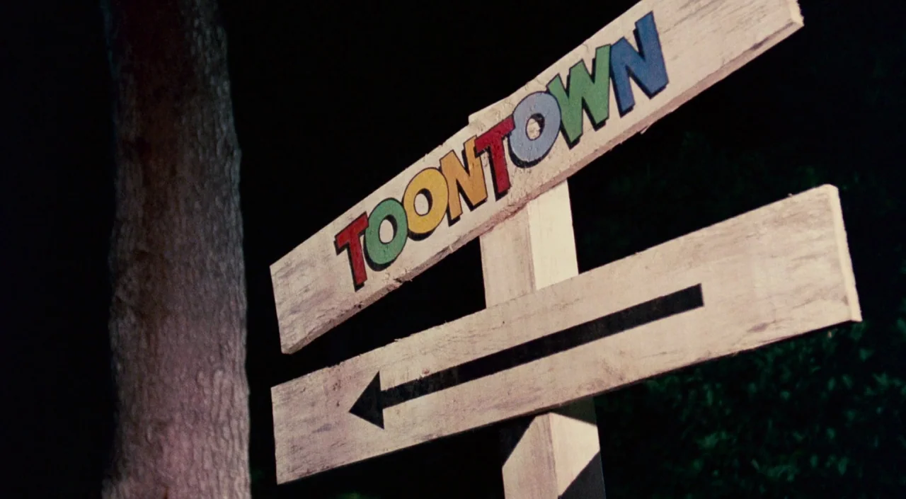 Who Framed Roger Rabbit (1988) movie still: closeup — A wooden directional signpost points the way toward Toontown in a dark nighttime setting. The…